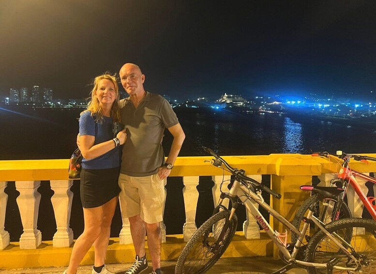 Two people standing on a bridge with a cityscape and a river in the background. 5