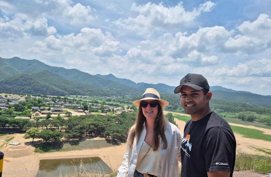 Two people standing by a scenic overlook with a view of a village and mountains in the background. 5