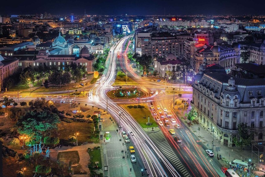 A nighttime cityscape with a prominent roundabout, illuminated buildings, and a mix of vehicular traffic. 3