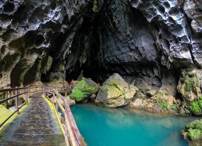 A cave with a turquoise pool and a wooden staircase leading down. 5