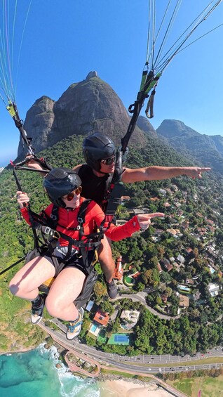 Two people paragliding with a mountainous landscape and a coastal town below. 4
