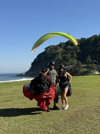 A person preparing to launch a paraglider with a green canopy, standing on a grassy field with a coastal cliff in the background. 2