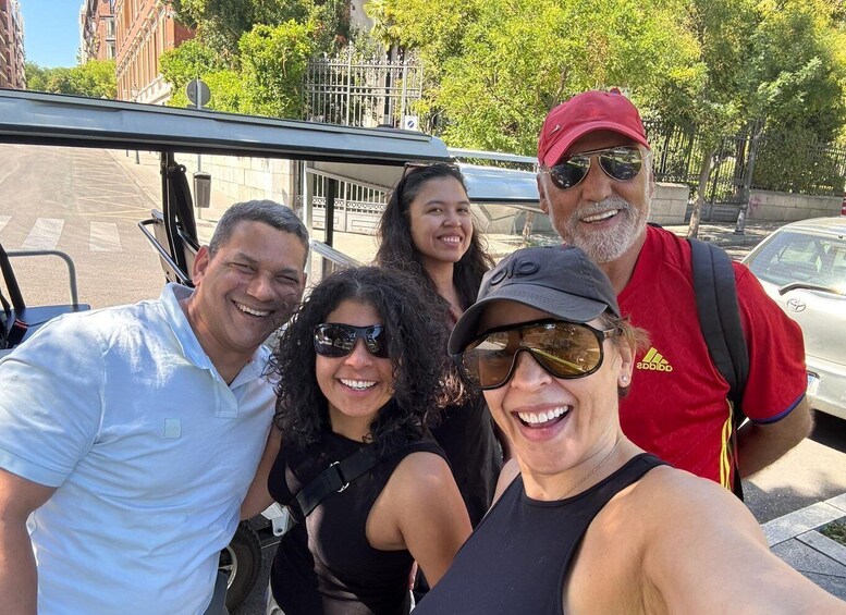A group of people posing for a selfie on a city street with buildings and trees in the background. 3