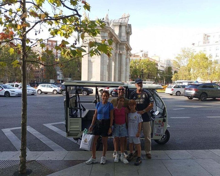 A group of people posing with a golf cart on a city street. 2