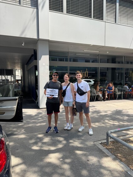 Three people standing in front of a building with a sign that reads 'EMO TOURS SWISS.' 3