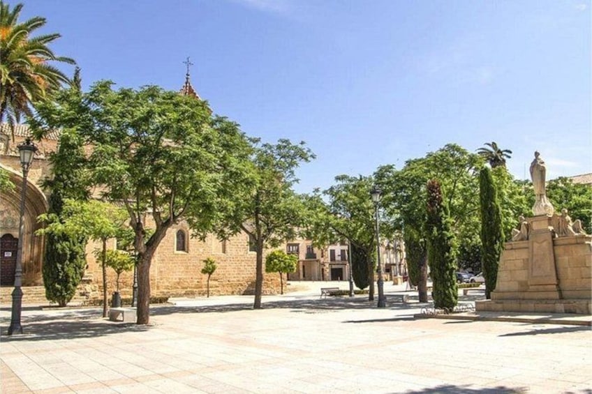 A courtyard with a church, trees, and a statue. 4