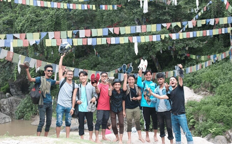 A group of people standing on a rocky outcrop with colorful prayer flags strung above them. 2