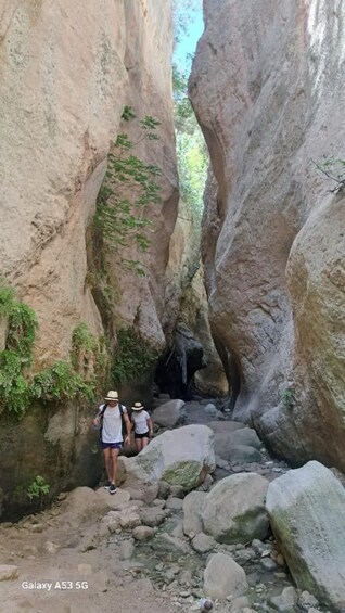 Hikers walking through a narrow canyon with large rock formations and a small waterfall. 4