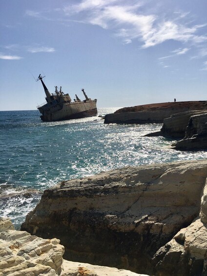 A shipwreck on a rocky coastline with clear blue water and a person standing on the rocks in the background. 2