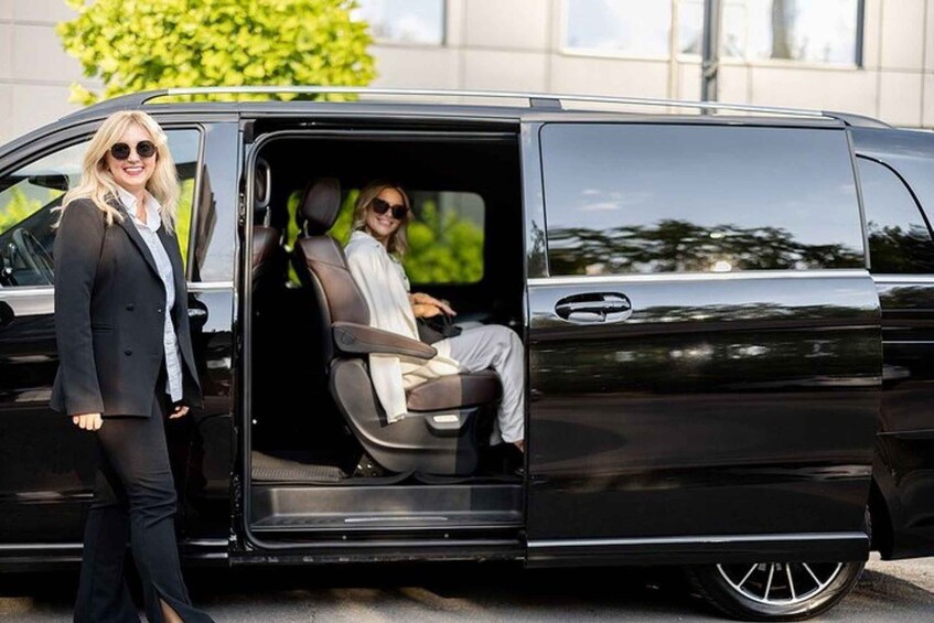 A black van with its door open, revealing a person inside wearing a white shirt and light-colored pants. 1