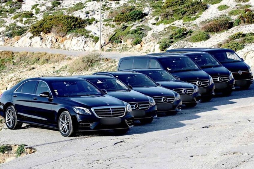 A row of parked Mercedes-Benz cars on a gravel road with a rocky hillside in the background. 4