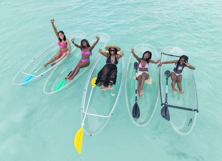 Five people on transparent paddleboards in turquoise water. 2