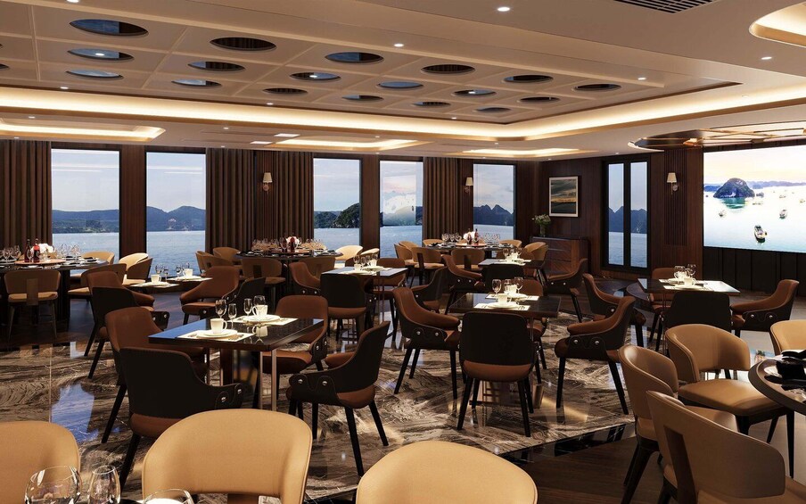 A spacious dining area with multiple tables and chairs, large windows overlooking a body of water. 3