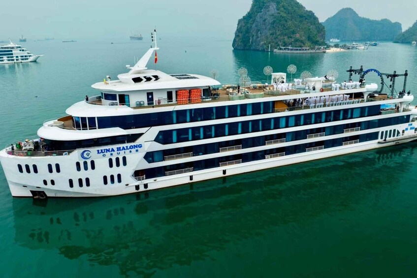 A large white cruise ship named Luna Balong cruising in a body of water with a mountainous island in the background. 1