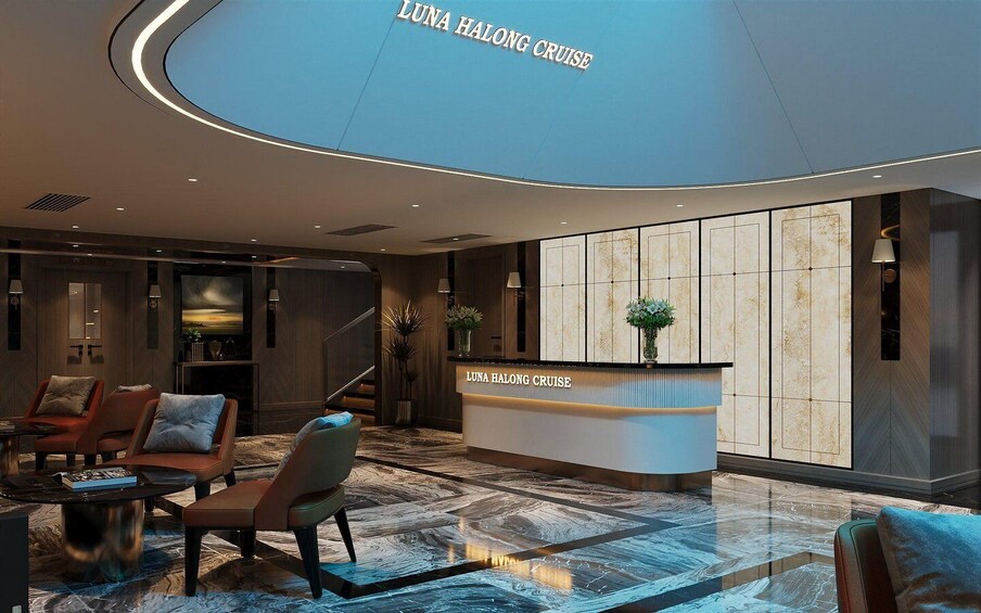 A modern lobby with a reception desk labeled 'LUNA HALONG CRUISE'. There are leather chairs, a marble floor, and a large wall with a vertical panel design. 4