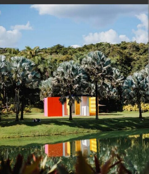 A modern building with red and yellow walls, surrounded by palm trees and a pond reflecting the structure. 3
