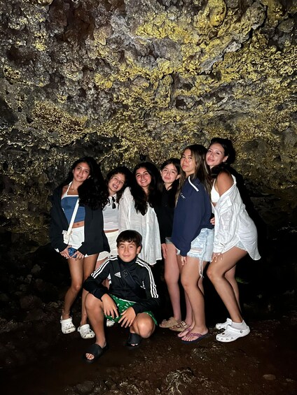 A group of people posing in front of a cave with golden lichen. 2