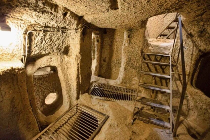 A stone-walled room with a ladder, a metal grate, and a circular opening. 5