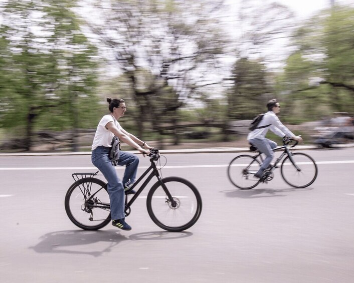 Two cyclists on a road with trees in the background. 2
