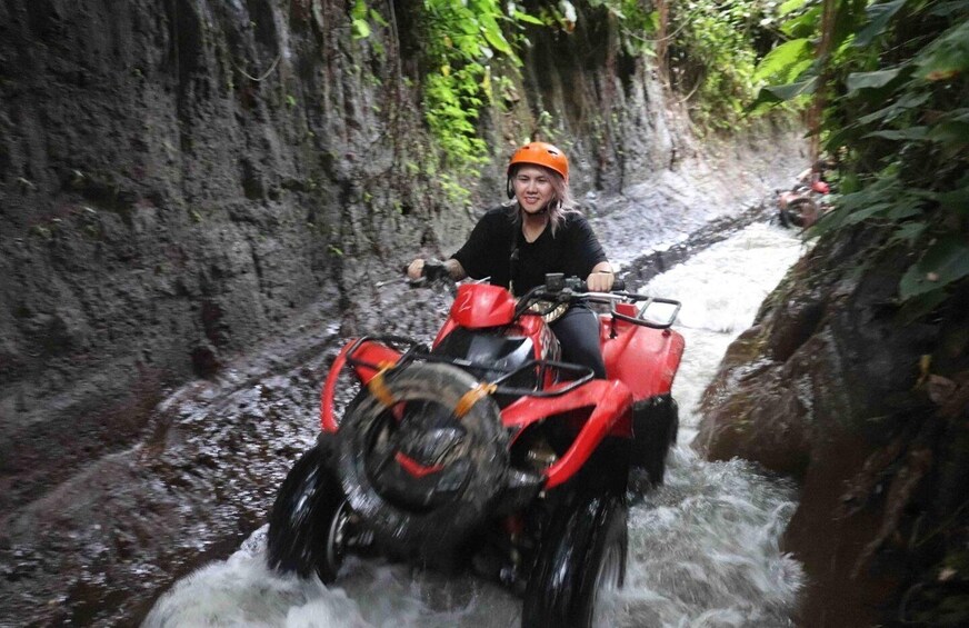 Une personne conduit un quad rouge dans un étroit canal rocheux rempli d’eau, le tout étant entouré d’une végétation dense. 4