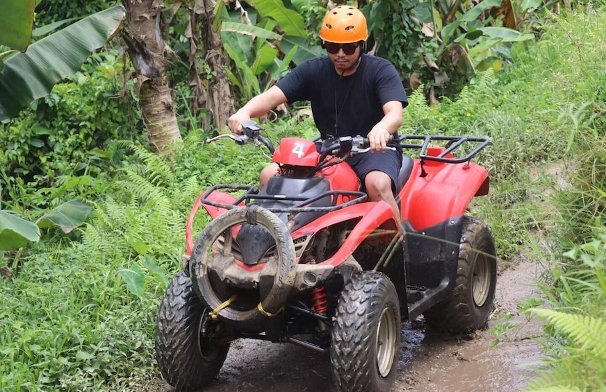 Une personne conduit un quad rouge sur un sentier boueux, entourée d’une végétation luxuriante. 1
