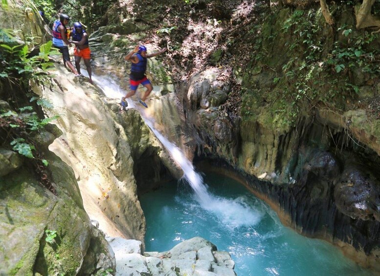 A group of people crossing a narrow water gap on a rocky path in a forested area. 3
