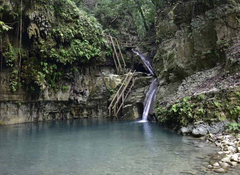 A waterfall cascading into a clear pool surrounded by rocky cliffs and lush greenery. 1