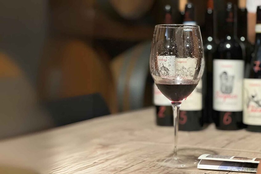 A glass of red wine on a wooden table with blurred wine bottles in the background. 4