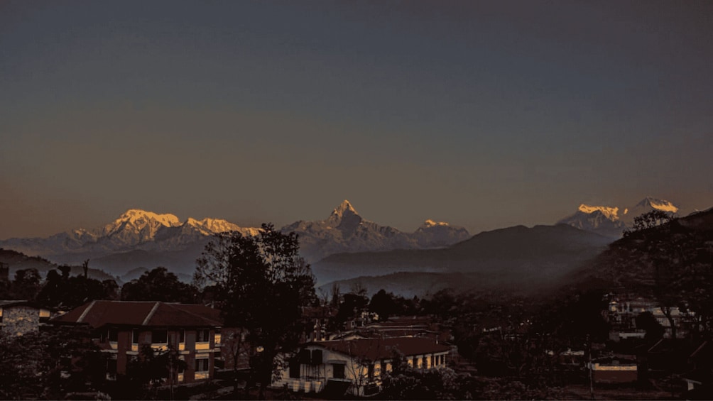 A mountain range with snow-capped peaks, a village with houses, and a clear sky. 2