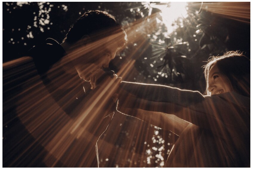 Two people holding hands with sunlight filtering through trees. 2
