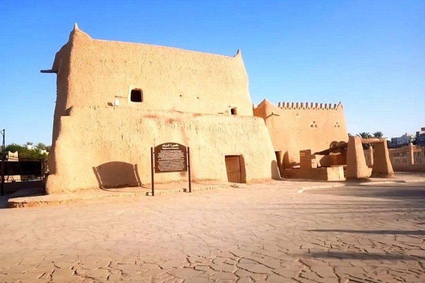Un edificio histórico con un letrero, una zona pavimentada y cielo despejado. 1
