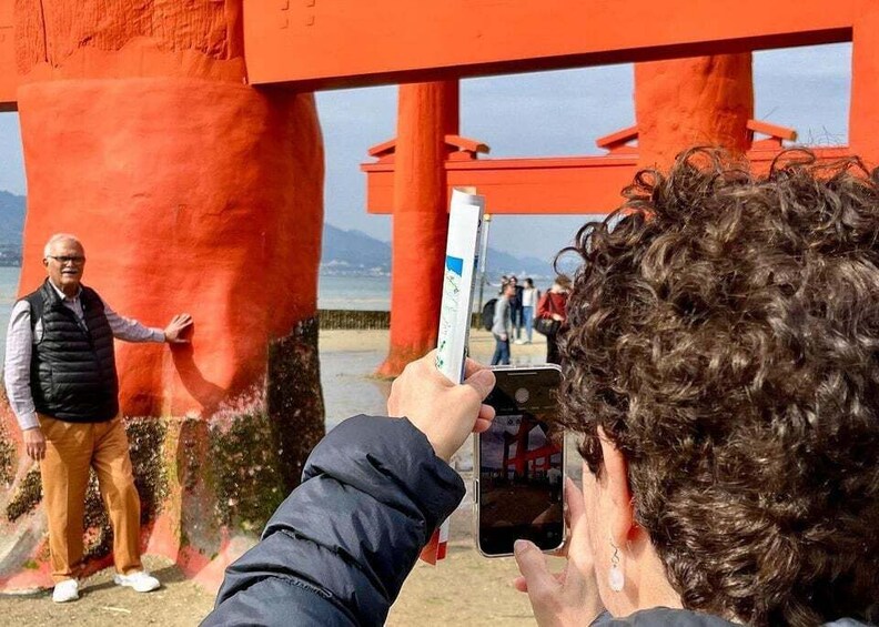 A person taking a photo of a red structure with a person in the background. 1