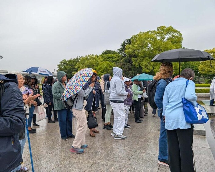 A group of people standing in a line outdoors, some holding umbrellas. 5