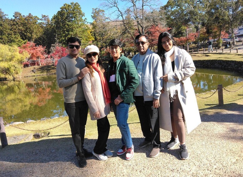 A group of people standing by a pond with autumn foliage in the background. 3