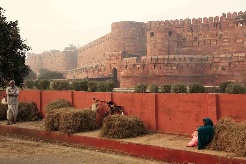 A large red wall with hay bales and a bicycle in front of a historic fort. 4