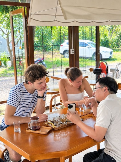 Three people sitting at a wooden table with drinks and a coffee pot. 2