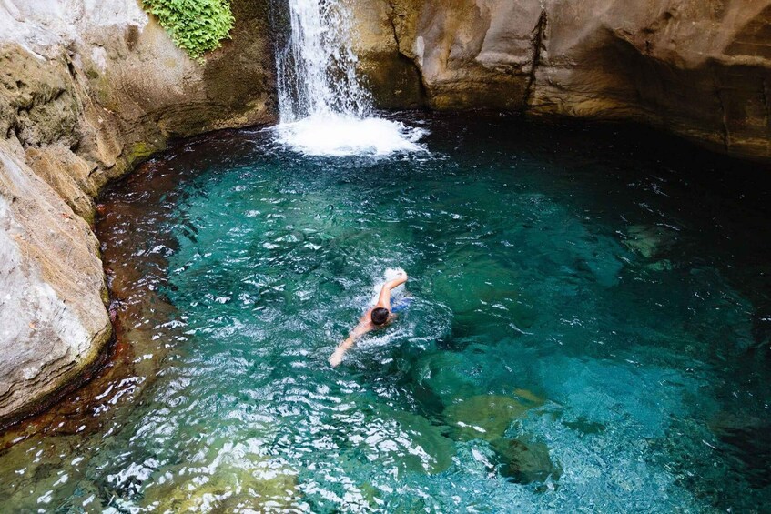 A person swimming in a clear blue pool with a waterfall. 5