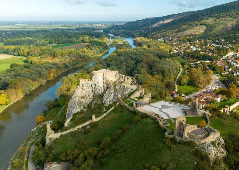 An aerial view of a historic castle surrounded by a river and lush greenery, with a small town in the background. 1