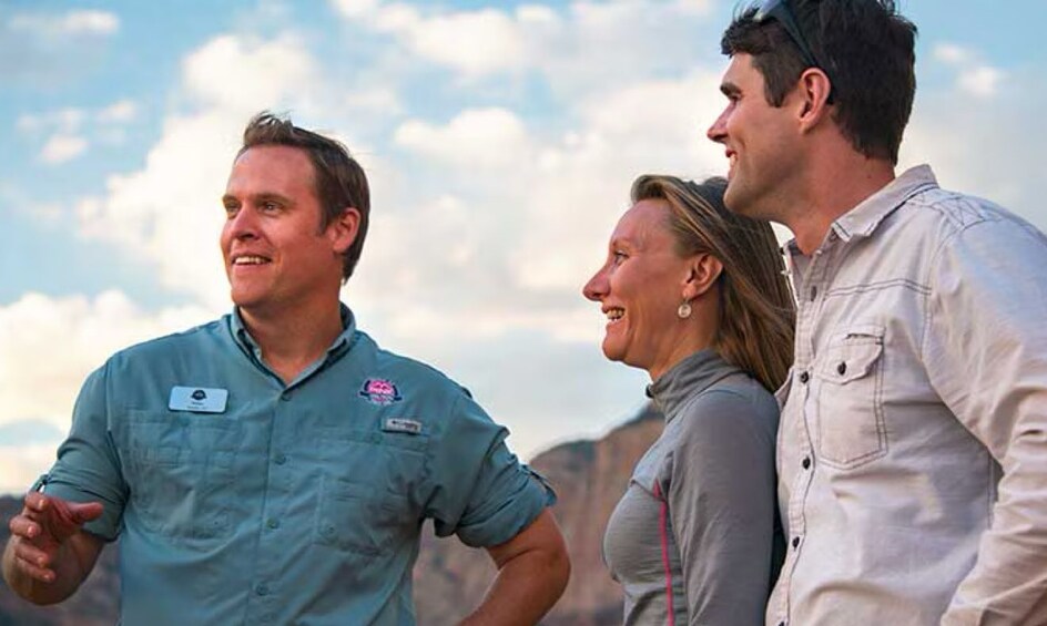 Three people outdoors, one in a blue shirt and another in a white shirt, with a mountainous landscape in the background. 3