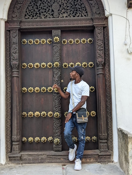 A man standing in front of a large ornate wooden door with brass flower-shaped handles. 1
