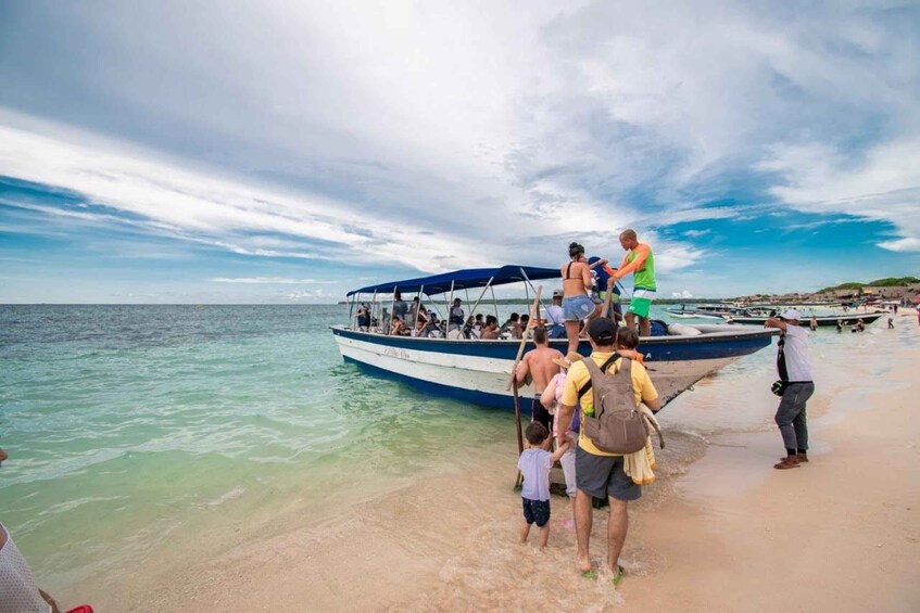 A crowded beach with people boarding a boat. 2