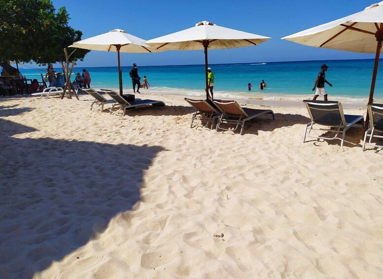 A beach with sun loungers and umbrellas, people walking and swimming in the water. 3