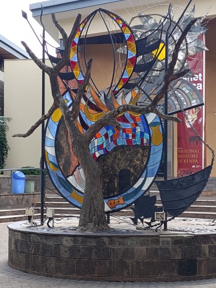 A colorful mosaic sculpture with a tree in the foreground. 1