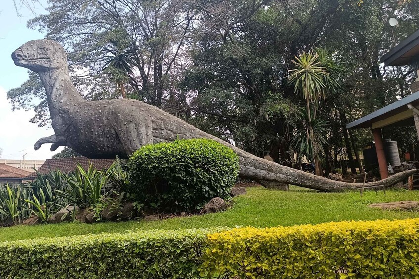 A large dinosaur statue in a park with green grass, bushes, and trees. 4