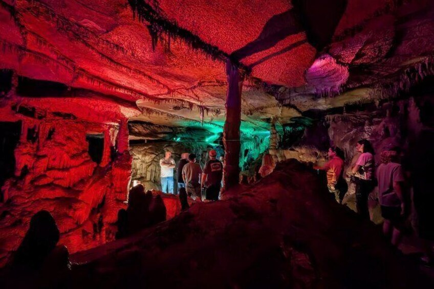 Una cueva con iluminación roja y verde, estalactitas y gente explorando. 3