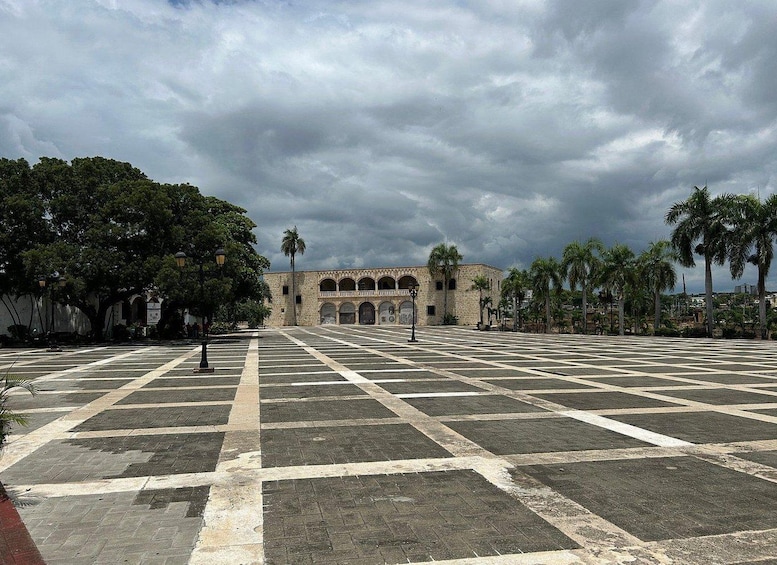 A plaza with a patterned pavement, palm trees, and a historic building with arches. 2