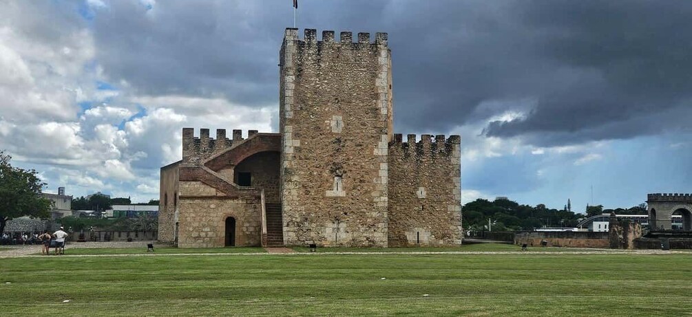 A historic stone tower with battlements, a grassy field in the foreground, and a cloudy sky. 3