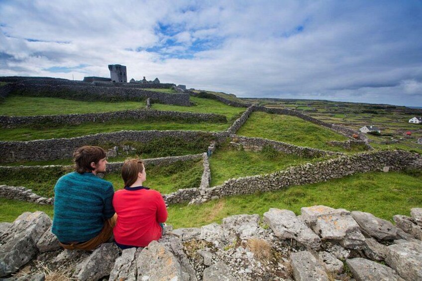 Dos personas sentadas sobre un muro de piedra con vistas a un lugar histórico con ruinas y muros de piedra. 3