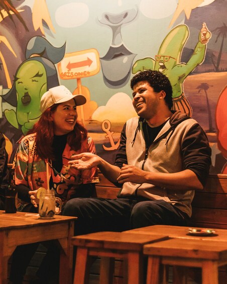 Two people sitting at a table in a restaurant with a mural in the background. 2