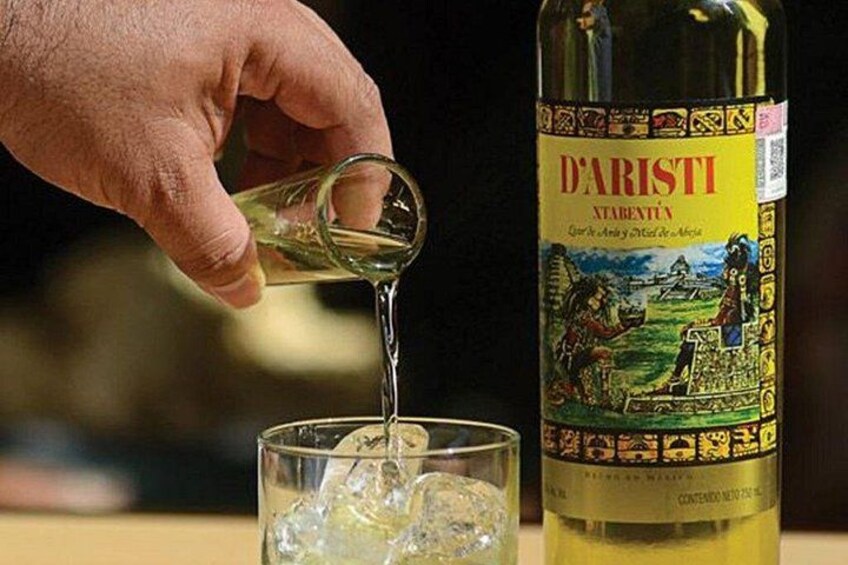 A hand pouring a clear liquid into a glass with ice cubes. A bottle labeled 'D'ARISTI' is visible in the background. 3
